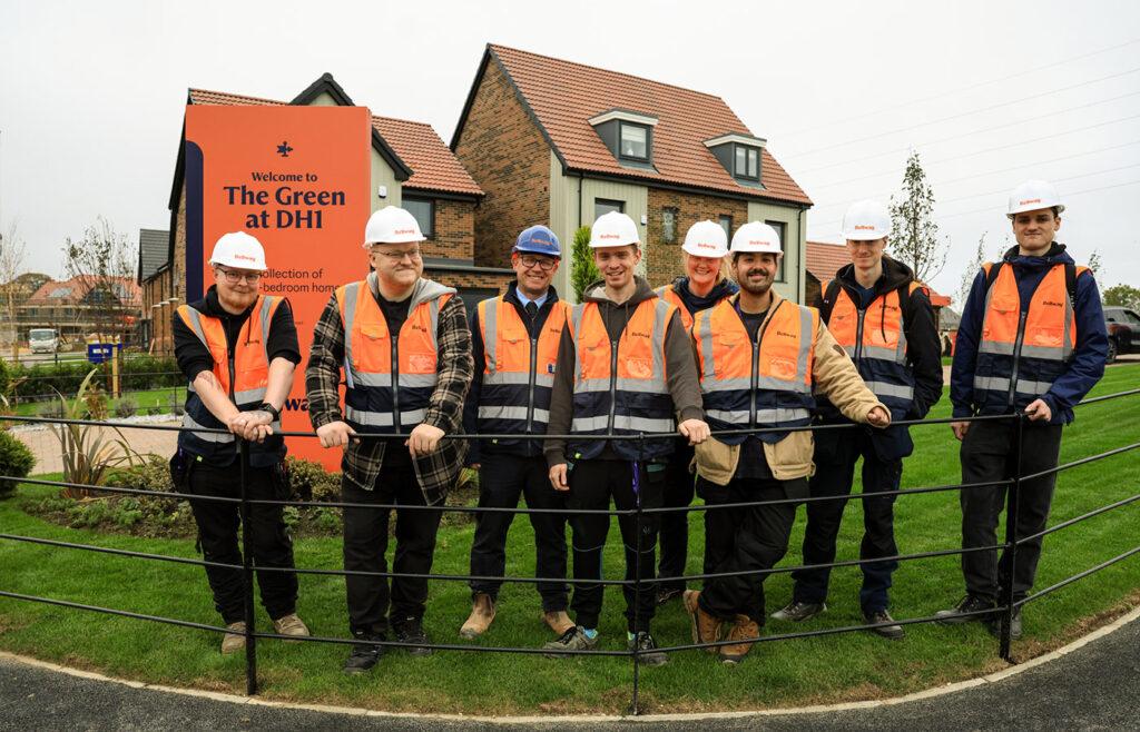 Bellway Site Manager Christopher Clough (blue hard hat) at the entrance of The Green at DH1 with some of the students who took part in the visit.